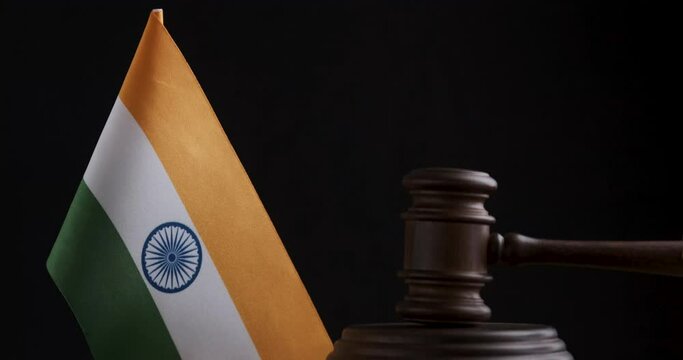 Judge's hammer hits the shock block near the Indian flag, black background. Wooden Mallet next to India flag.