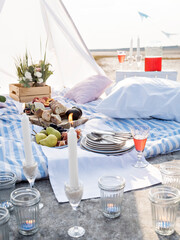 Summer brunch or dinner organised on a sea shore for friends. Elegant decorated place for romantic date. Sun lit flowers, fruits, cheese and bread as a snacks, candles.Festive and stylish tableware.