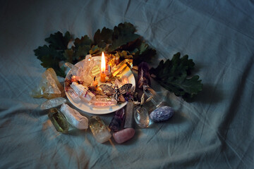 gemstones, candle, amulet, leaves on fabric abstract dark background. witch Esoteric spiritual...