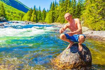 Young man on rock in river Rjukandefossen waterfall Hemsedal Norway.