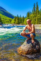 Young man on rock in river Rjukandefossen waterfall Hemsedal Norway.