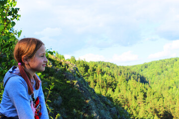 Naklejka premium the girl sits alone on the edge of the cliff and looks at the river. the mountains. Forest. Mountain landscape through the foliage of trees. Breathtaking panoramic view from the top of the peak