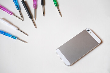 Multi-colored screwdrivers for phone repair and a gray smartphone on a white background, phone and equipment repair