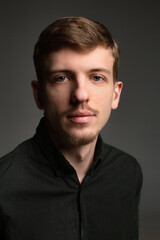 Obraz premium Portrait of young blond european man with short beard and mustache isolated on dark grey in black clothes