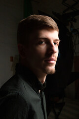 Fototapeta premium Portrait in shadow of young blond european man with short beard and mustache isolated on black