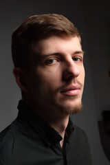 Fototapeta premium Portrait in shadow of young blond european man with short beard and mustache isolated on black