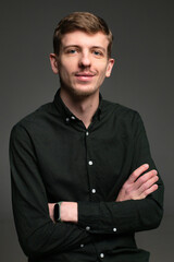 Smiling young blond european man with short beard and mustache isolated on dark grey with folded arms