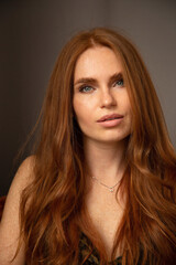 Fototapeta premium Portrait of woman with long red hair in animal print dress with gray eyes in dark room