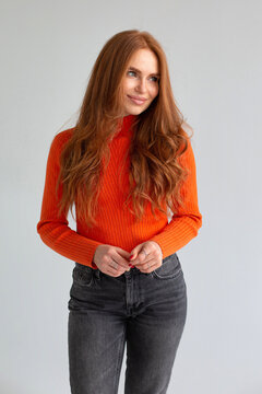 Shy Woman With Long Red Hair In Orange Jumper Isolated On Light Grey