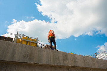 Builder in a hardhat and a vest on a concrete structure against the sky