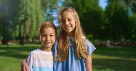 Smiling girl hug little brother looking in camera. Boy unwilling to embrace.