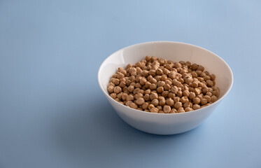 Selected grains of raw chickpeas in a white bowl on a blue background. Horizontal orientation, copy space, no people