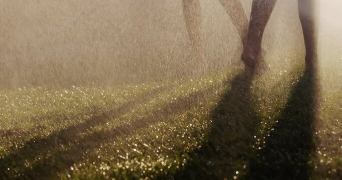 Two barefoot women run on the green grass in jets of water. Slow motion 4k video. Youth and health concept