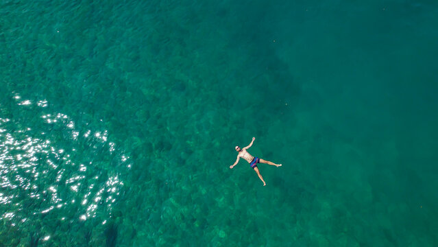 TOP DOWN: Flying above a relaxed male tourist floating on his back during a swim