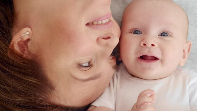 Happy newborn baby with his mother.  Healthy newborn baby in a white t-shirt with mom.   Closeup Faces of the mother and infant baby. Cute  Infant boy and parent, top view.  Slow motion. Happy family