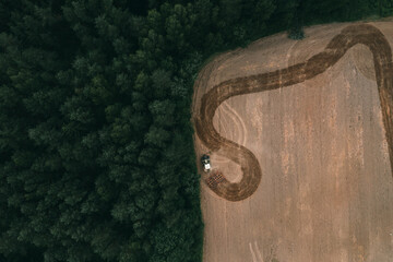 Aerial view of arable land with traces of tire harrows and tractors. Patterns on the ground. Green forest