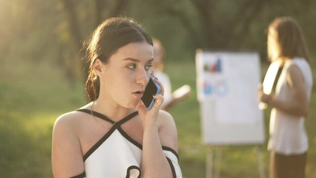 Bored Annoyed Beautiful Woman Talking On Phone Rolling Eyes Looking Back At Colleagues Discussing Business In Park At Golden Sunset. Portrait Of Irritated Caucasian Employee At Outdoors Team Building