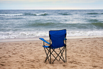 Blue folding chair back on sea beach, without people, beach holiday alone, loneliness