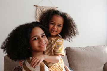 Younger and older sister spending time together at home. Two black girls of different age hugging...
