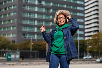 Fototapeta premium Portrait of young attractive black girl in urban background hearing music with headphones