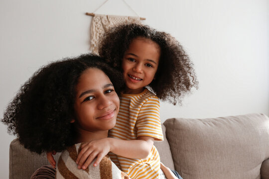 Younger and older sister spending time together at home. Two black girls of different age hugging and showing affection. Black female siblings having fun and bonding. Background, copy space, close up.