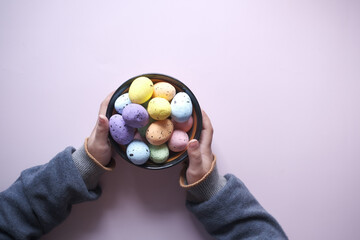 child hand holding a bowl of easter eggs on pink 