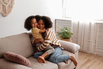 Younger and older sister spending time together at home. Two black girls of different age hugging and showing affection. Black female siblings having fun and bonding. Background, copy space, close up.