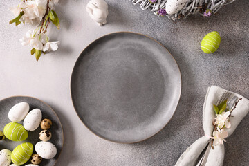 Easter table setting with gray plate, spring blossom flowers and white green eggs on gray background. View from above.