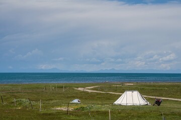The blue sky and white clouds beside Qinghai Lake, as well as some tents and prayer flags on the grassland