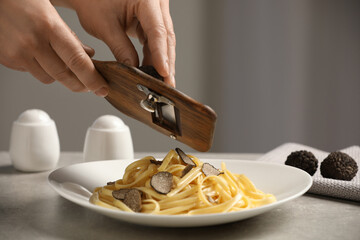 Woman slicing truffle onto fettuccine at grey table, closeup