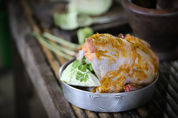 Whole Raw Chicken in iron pan marinated and ready to cook with ingredients for cooking. on wooden table.
