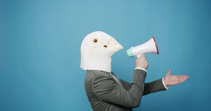 Guy in gray suit with Pigeon Mask on blue Background Talking on the megaphone. proclaiming the news, loudly announcing the advertisement, warning using the loudspeaker to shout. Fool's Day. 
