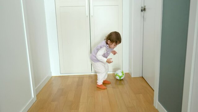 Multi-ethnic two-year old toddler girl picks up a soccer ball to play with - slow motion