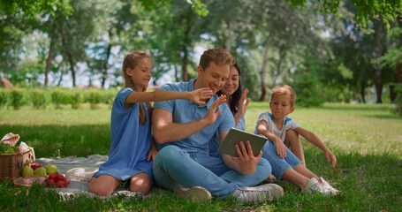Smiling family waving hands communicate using tablet on nature in summer day.