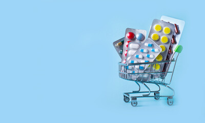 On a light blue background, a shopping trolley with pills. Medical concept. Copy space