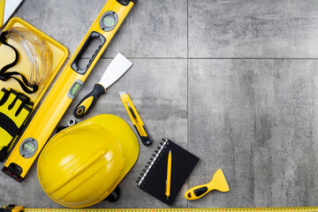 Contractor theme. Tool kit of the contractor: yellow hardhat, libella, hand saw. Plans and notebook on the gray tiles.