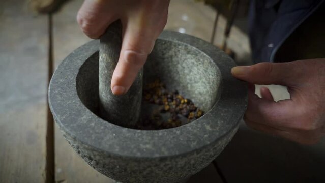 Old male hands triturating  juniper in stone mortar