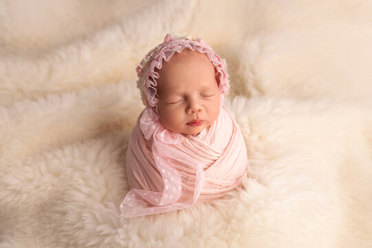 Sleeping newborn girl in the first days of life in a pink cocoon with a pink cap on a white background. Studio macro photography, portrait of a newborn baby. The concept of female happiness.
