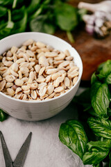 Photo of a fresh healthy ingridients like green basil, fresh garlic, roast nut, parmegiano cheese to make homemade pesto sauce on a wooden desk indoors daylight