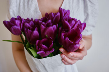 Happy woman holds purple tulips in her hands. Florist girl gathered a bouquet. Beautiful lavender flowers. Blossom petal. Gift for the holiday celebration, springtime mood. Romantic surprise