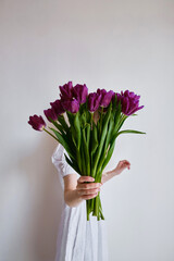 Happy woman holds purple tulips in her hands. Florist girl gathered a bouquet. Beautiful lavender flowers. Blossom petal. Gift for the holiday celebration, springtime mood. Romantic surprise
