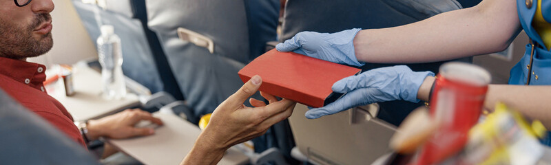 Close up shot of hands of male passenger getting lunch box from female flight attendant serving food on board. Travel, service, transportation, airplane concept