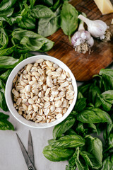 Photo of a fresh healthy ingridients like green basil, fresh garlic, roast nut, parmegiano cheese to make homemade pesto sauce on a wooden desk indoors daylight