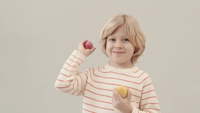 Medium slowmo portrait of 7-year-old Caucasian boy smiling at camera shaking Easter eggs in hands standing on clear background