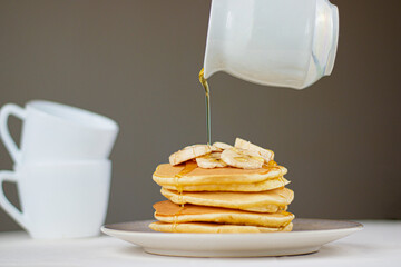 Pancakes with honey. A stack of banana pancakes with slices of fresh bananas  and honey on top with cup of tea on a wooden background. A healthy breakfast. copy space

