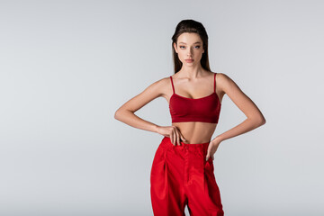 pretty model in red outfit posing with hands on hips isolated on grey.