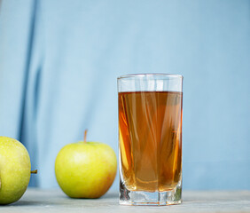 Glass of apple juice with apples on a wooden table, close-up.