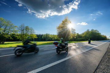 Three motion blurred motorcycles riding on the asphalt road along a spring meadow in the woods at...