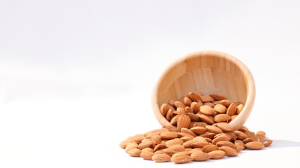 close up of organic brown raw almond seed heap with wooden circle bowl on white background. healthy nuts eating and kernel concept
