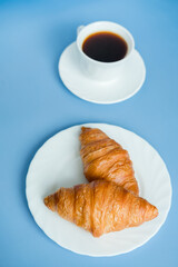 Croissants and morning coffee in a white cup on a blue background, top view